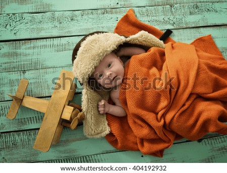 Baby boy aviator with pilot scarf and hat and handmade toy airplane over vintage wooden background