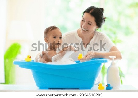 Baby boy in bath. Mother washing infant child. Cute little toddler playing with soap foam in white sunny bathroom. Water fun. Hair and skin care for young kids. Shampoo and body lotion. Bath toys.