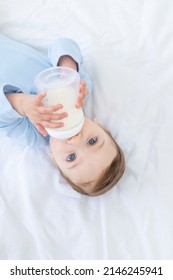 niño bebé con una botella de leche en la cama antes de acostarse con un traje corporal azul, concepto de comida para bebé