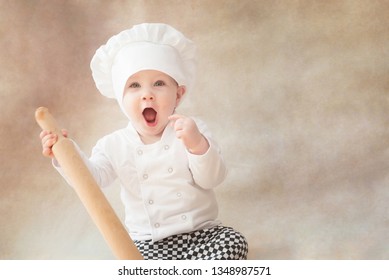 Baby boy, child in chef costume cook with rolling pin. Positive