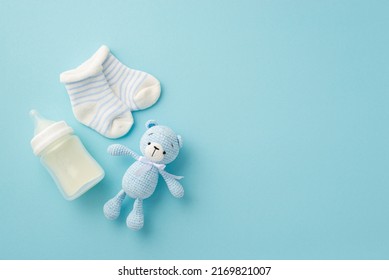 Baby boy concept. Top view photo of tiny socks milk bottle and knitted teddy-bear toy on isolated pastel blue background