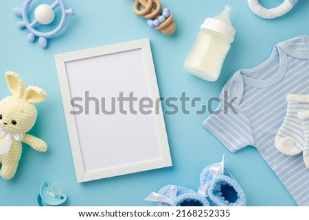 Baby boy concept. Top view photo of photo frame knitted bunny toy blue shirt socks milk bottle teether wooden rattle shoes and baby's dummy on isolated pastel blue background with empty space