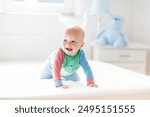 Baby boy crawling on bed. Little child playing in white sunny bedroom. Infant kid learning to crawl. Nursery for children. Textile, clothing and bedding for kids. Family morning at home.