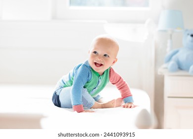 Baby boy crawling on bed. Little child playing in white sunny bedroom. Infant kid learning to crawl. Nursery for children. Textile, clothing and bedding for kids. Family morning at home. - Powered by Shutterstock