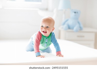 Baby boy crawling on bed. Little child playing in white sunny bedroom. Infant kid learning to crawl. Nursery for children. Textile, clothing and bedding for kids. Family morning at home. - Powered by Shutterstock