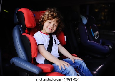 Baby Boy With Curly Hair Sitting In Red Child Car Seat In A Minivan.