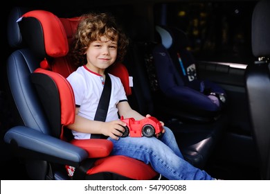 baby boy with curly hair sitting in a child car seat with toy car in the hands of