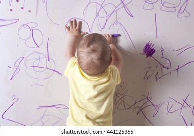 Baby Boy Drawing With Wax Crayon On Plasterboard Wall. He Is With His Back Towards