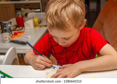 Baby boy draws a man with pencils and markers. The child sits at the laptop and paints a picture. The boy stuck out his tongue in exertion. Hardworking kid.