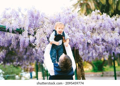 Baby boy is flying in his father's arms under a wysteria tree