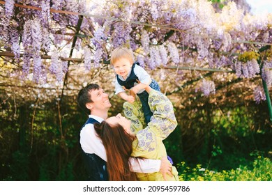 Baby boy is flying in his mother's arms under a wysteria tree on a sunny day