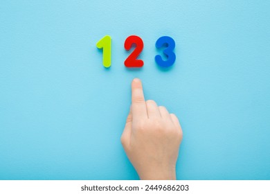 Baby boy hand finger pointing to colorful 123 numbers on light blue table background. Pastel color. Time to learning. Closeup. Top view. - Powered by Shutterstock