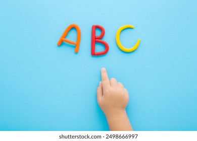 Baby boy hand finger pointing to colorful abc letters created from modeling clay on light blue table background. Pastel color. Time to learning. Closeup. Top view. - Powered by Shutterstock