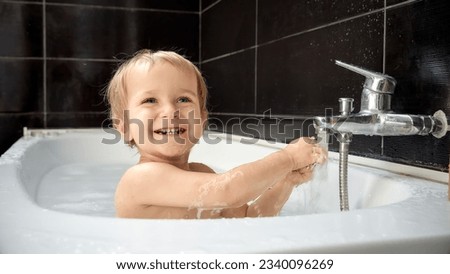 Baby boy having fun in the bath and splashing around water from faucet. Keeping babies clean and healthy