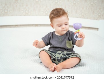 Baby boy with his first toys. Charming blond child playing with toy rattle sitting on a bed