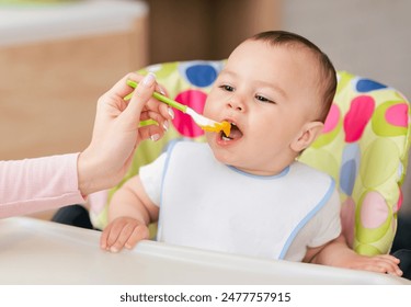 A baby boy is in his high chair enjoying a meal as his mom feeds him. The kitchen setting is comfortable and bright, showcasing a caring and loving interaction. - Powered by Shutterstock