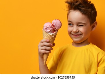Baby boy kid eating strawberry ice cream in waffles cone and winking on yellow background with free text copy space