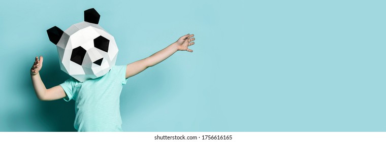 Baby boy kid in polygonal panda mask dancing with hands spread up popular sign on pastel color blue mint background. Banner with text copy space