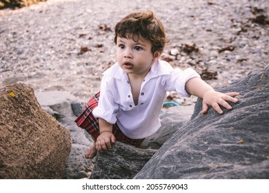 Baby boy in kilt climbing rocks
