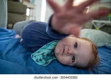 Baby Boy Laying On The Floor Reaching Hand Toward Camera.