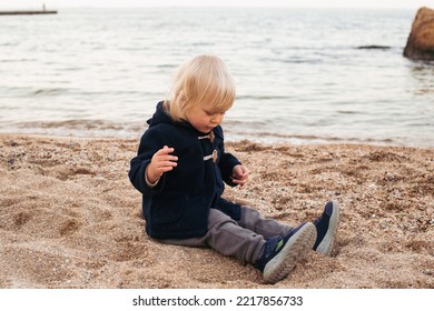 Baby Boy On The Beach Near Sea. Child On Vacation In Summer Or Autumn At The Sea On Bad Weather In Autumn Or Summer Time