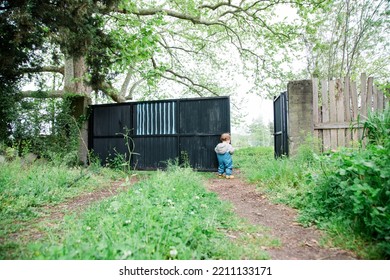 A Baby Boy Is Opening Garden Door, He Is Wearing Gardening Jump Suit. Background Is Pure Natural Green (no Face- Back Side Of The Baby Boy)