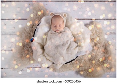A baby boy is peacefully sleeping during his first professional photo-shoot. He is dressed in white and covered with a white blanket.