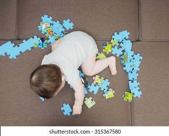 Baby boy playing with puzzle pieces on a sofa at home
