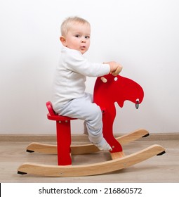 Baby boy playing with a rocking horse on grey background