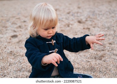 Baby Boy Playing With Sand On The Beach Near Sea In Autumn Or Summer Time