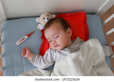 Baby boy sick sleep in cot next to digital thermometer. Mixed race Asian-German infant sickness, fever lying on bed.