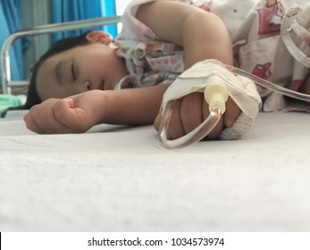 Baby Boy Sick And Sleeping On Patient Bed At The Hospital. Saline Intravenous Or (IV)drip In Baby Patient Hand. Poor Baby Looks Tired And Exhausted.IV Fluid Replacement Or Correcting The Dehydration