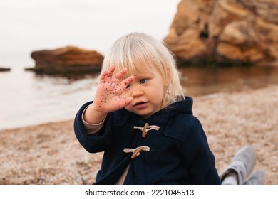 Baby Boy Sitting On The Beach Near Sea In Autumn Or Summer Time