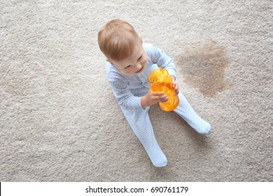 Baby Boy Sitting On Carpet With Empty Glass Near Wet Spot