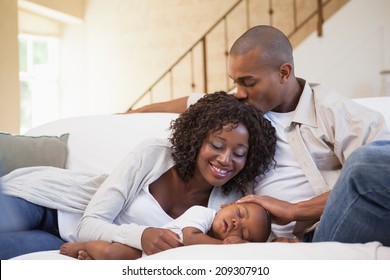 Baby boy sleeping peacefully on couch with happy parents at home in the living room - Powered by Shutterstock