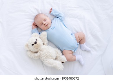 baby boy sleeps on the bed lying on his back with a soft toy bear in blue pajamas holding his hands up, healthy newborn sleep