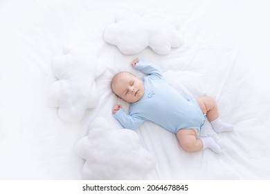 baby boy sleeps on the bed lying on his back in blue pajamas with his hands up among the pillows of clouds, healthy newborn sleep - Powered by Shutterstock