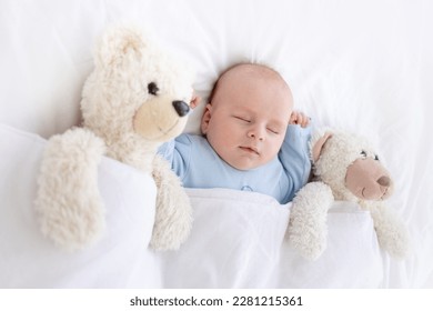 baby boy sleeps on the bed lying on his back with a soft toy bear in blue pajamas holding his hands up, healthy newborn sleep