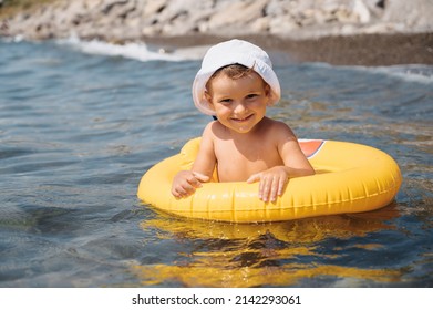 Baby boy swims with an inflatable yellow circle in the sea on a sunny day. The kid learns to swim and enjoys the game.