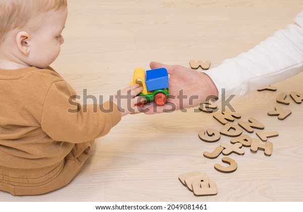 Baby boy\
takes a toy car from the hands of dad sitting on the wooden floor.\
Nearby are the letters of the English alphabet. Early development,\
parent-child relationship concept.\
