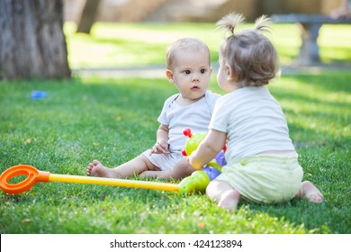 Baby boy and toddler girl playing while sitting on green grass in park
