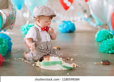 Baby boy touching his first birthday cake. Making messy cakesmash in decorated studio location.
