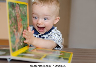 Baby Boy Turns The Page In The Book With Animal. He Is Very Happy And Excited By Watching Pictures. Child Concept.