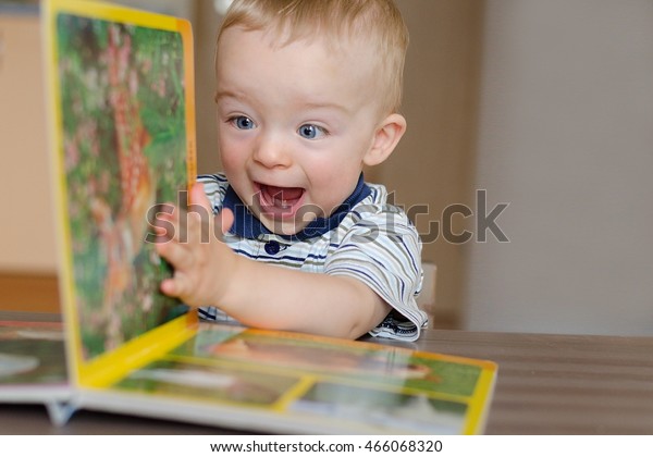Baby boy\
turns the page in the book with animal. He is very happy and\
excited by watching pictures. Child\
concept.
