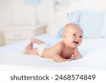 Baby boy wearing diaper in white sunny bedroom. Newborn child relaxing in bed. Nursery for children. Textile and bedding for kids. Family morning at home. New born kid during tummy time with toy bear.