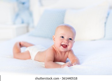 Baby boy wearing diaper in white sunny bedroom. Newborn child relaxing in bed. Nursery for children. Textile and bedding for kids. Family morning at home. New born kid during tummy time with toy bear.