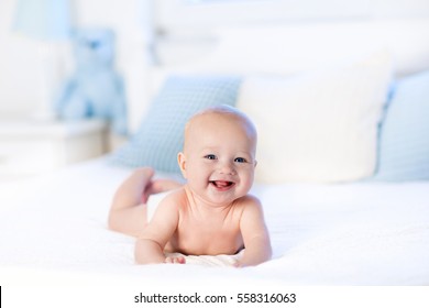 Baby boy wearing diaper in white sunny bedroom. Newborn child relaxing in bed. Nursery for children. Textile and bedding for kids. Family morning at home. New born kid during tummy time with toy bear