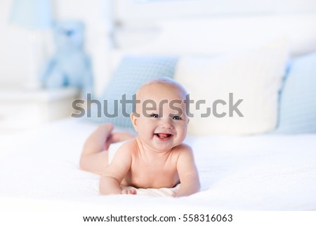 Baby boy wearing diaper in white sunny bedroom. Newborn child relaxing in bed. Nursery for children. Textile and bedding for kids. Family morning at home. New born kid during tummy time with toy bear
