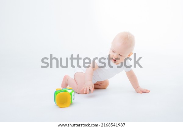  baby boy in a white bodysuit is sitting
playing  with toy cars on white
background