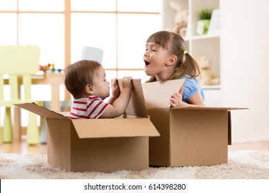 Baby Brother And Child Sister Playing In Cardboard Boxes In Nursery